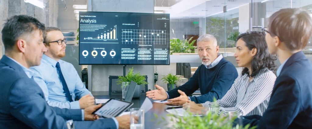 people meeting around table with large monitor at end