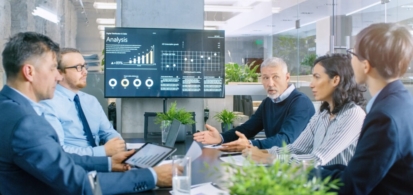 people meeting around table with large monitor at end