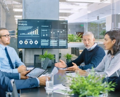 people meeting around table with large monitor at end