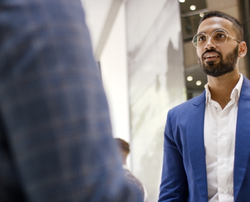 Two business people talking, wearing suits, including a man of Indian descent