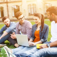 A diverse group of students demonstrating the results of simplifying SaaS adoption, gather outside a university building, looking at a laptop and each other