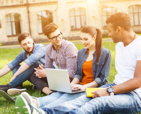 A diverse group of students demonstrating the results of simplifying SaaS adoption, gather outside a university building, looking at a laptop and each other