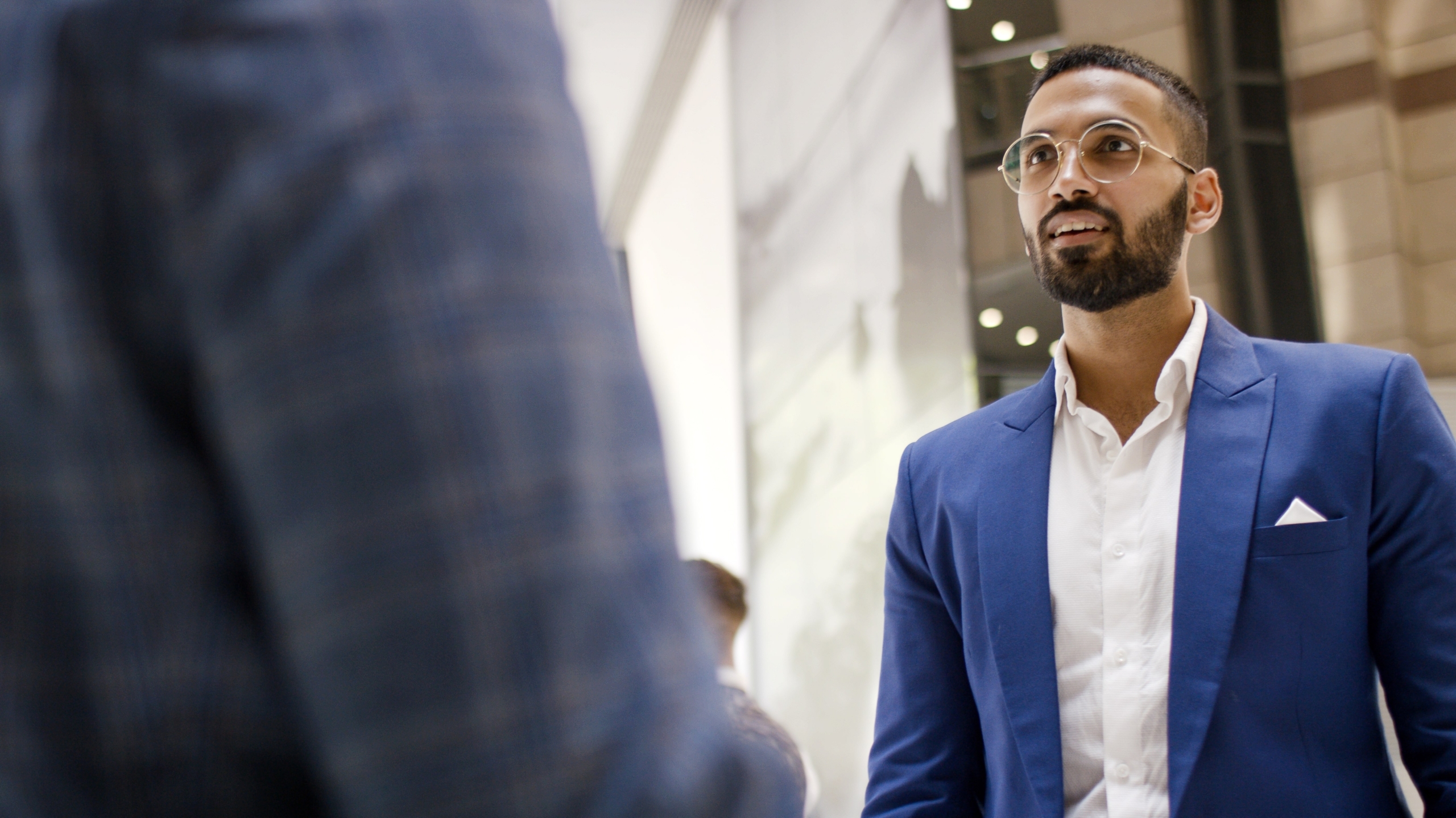 Two business people talking, wearing suits, including a man of Indian descent